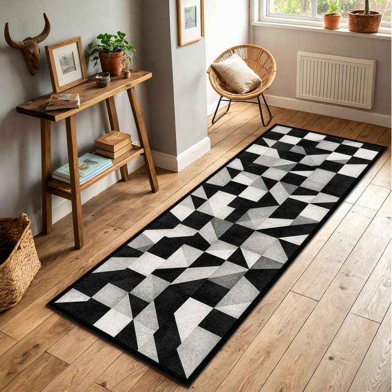 May include: A long, rectangular rug with a geometric pattern in black, white, and grey. The design features a repeating pattern of triangles and squares, creating a modern, abstract look. The rug has a black border and is placed on a wooden floor.