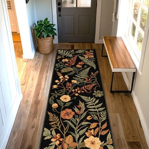 Pu&ograve; includere: Un lungo tappeto nero rettangolare con un disegno floreale con fiori e foglie arancioni, gialli e verdi. Il tappeto &egrave; posto in un corridoio con pavimenti in legno e una porta sullo sfondo.