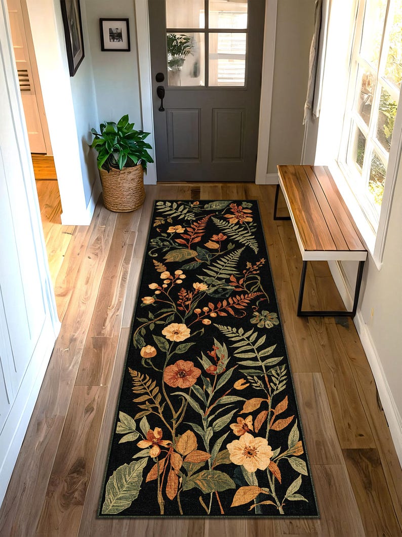 Pu&ograve; includere: Un lungo tappeto nero rettangolare con un disegno floreale con fiori e foglie arancioni, gialli e verdi. Il tappeto &egrave; posto in un corridoio con pavimenti in legno e una porta sullo sfondo.
