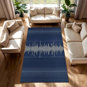 Può includere: Un tappeto rettangolare blu navy con un motivo a onde sonore bianco. Il tappeto, con strisce orizzontali, è collocato in una stanza con divani beige e piante, creando un moderno spazio abitativo.