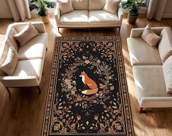 Puede incluir: Una alfombra rectangular negra con un borde floral detallado y un diseño central con un zorro. El zorro es naranja y blanco, rodeado por una corona floral. El diseño de la alfombra incluye flores y follaje de color naranja y crema.
