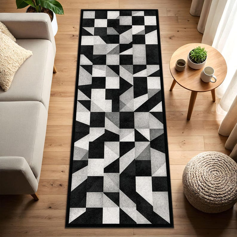 May include: A rectangular rug with a black and white geometric design. The rug has a repeating pattern of squares, triangles, and other shapes in shades of black, white, and grey. It is placed on a wooden floor.