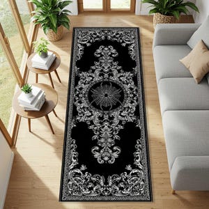 Op de afbeelding: Een zwart-wit decoratief loperkleed met een gotisch ontwerp. Het kleed heeft een centraal cirkelvormig ontwerp met een spinnenweb, omgeven door sierlijke krullen en bloemmotieven. Het kleed is rechthoekig.