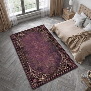 May include: A rectangular area rug featuring a deep plum and dark purple distressed base with a prominent ornate border. The border displays intricate gold and tan scrolling floral motifs and leaf patterns that frame the central field.