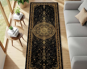 May include: Black rectangular rug with a gold celestial design. The rug features a central compass rose design, surrounded by stars, moons, and geometric patterns. The rug is placed on a hardwood floor, with a sofa and side tables in the background.