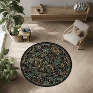 Op de afbeelding: Een ronde vloerkleed met een gedetailleerd bloemenontwerp in groen, goud en blauw op een zwarte achtergrond. Het vloerkleed ligt op een lichtgekleurde houten vloer, met een stoel en een houten kast op de achtergrond.