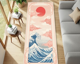 Puede incluir: Una alfombra rectangular con un diseño de inspiración japonesa. La parte superior representa un sol rojo y nubes rosas, mientras que la parte inferior muestra una gran ola azul y blanca. La alfombra está enmarcada con un borde rosa claro.
