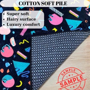 May include: A black rug with a colorful geometric pattern featuring pink circles, blue triangles, and yellow accents. The rug has a hairy surface and is labeled "COTTON SOFT PILE". The rug is described as super soft and providing luxury comfort.