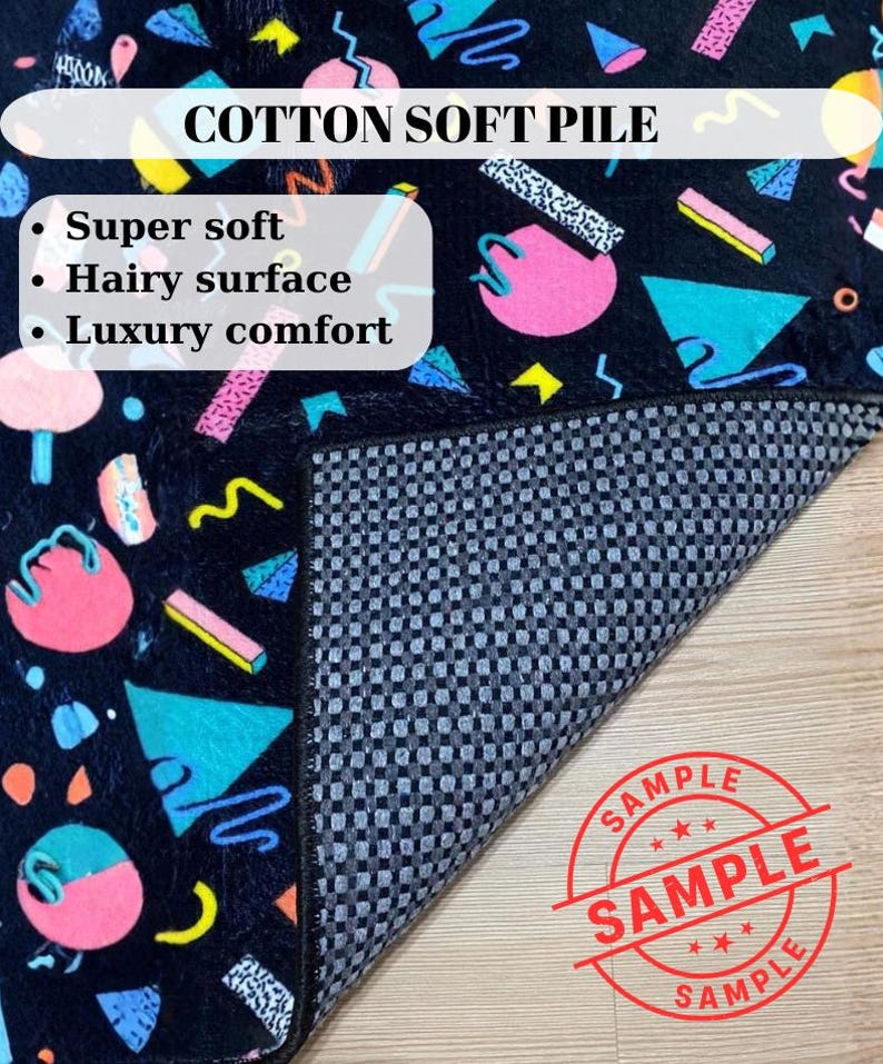 May include: A black rug with a colorful geometric pattern featuring pink circles, blue triangles, and yellow accents. The rug has a hairy surface and is labeled "COTTON SOFT PILE". The rug is described as super soft and providing luxury comfort.