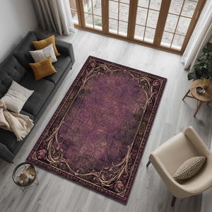 May include: A rectangular area rug featuring a deep plum and dark purple center with a distressed, weathered texture. The rug is framed by an ornate, light-colored border with intricate floral and scrolling vine patterns in a cream tone.