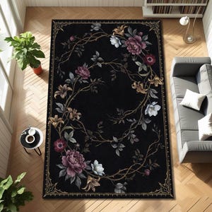 May include: A rectangular black area rug with a floral design. The rug features a central wreath of flowers in shades of purple, white, and gold, with a detailed border. The rug is placed on a wooden floor.