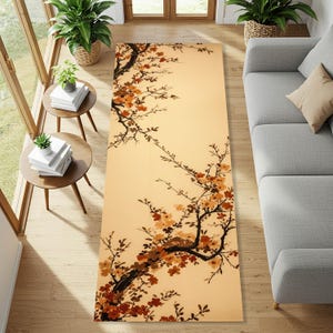 Könnte beinhalten: Ein rechteckiger Teppich mit beigem Hintergrund und einer detaillierten Illustration eines blühenden Astes in Braun- und Orangetönen. Der Teppich liegt auf einem Holzboden, mit einem grauen Sofa und Beistelltischen.