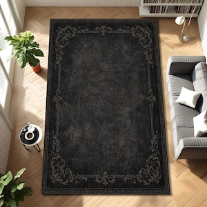 May include: A rectangular area rug featuring a dark charcoal black distressed texture with a decorative border of intricate light gray scrollwork and floral motifs framing the central field in a classic symmetrical pattern.