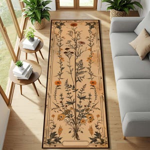 Puede incluir: Una alfombra rectangular con un diseño floral botánico. La alfombra presenta un fondo beige con un ramo central y bordes florales verticales en tonos de naranja, amarillo y marrón. Está enmarcada con un borde marrón oscuro.