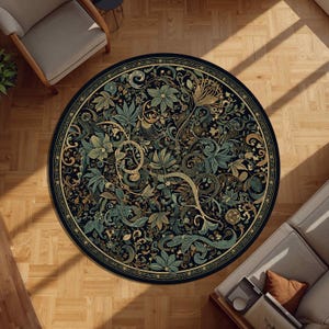 Op de afbeelding: Een rond vloerkleed met een gedetailleerd bloemenpatroon in tinten teal, goud en groen op een zwarte achtergrond. Het vloerkleed heeft een rand met een herhalend geometrisch ontwerp. Het ligt op een houten vloer.