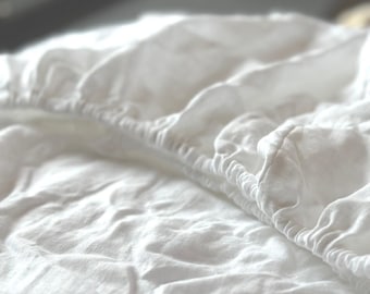 May include: Close-up of a white fitted sheet. The sheet is made of a soft, textured fabric and has an elasticized edge. The fabric is slightly wrinkled, suggesting it has been used or washed.