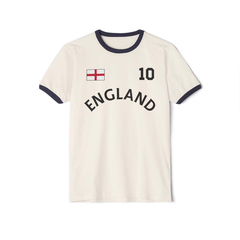 May include: A cream-colored ringer t-shirt with dark navy blue trim on the collar and sleeves. The front features a small England flag, the number 10 in black, and the word ENGLAND printed in a black, arched, sans-serif font across the chest.