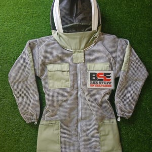 Puede incluir: Traje de apicultura de cuerpo entero con cuerpo y capucha de malla. El traje tiene detalles en verde oliva en los bolsillos, el cuello y los puños. Tiene una cremallera y un parche que dice "BEE STUFF ENTERPRISES".