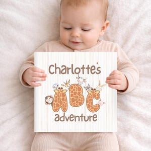 May include: A wooden sign with the text "Charlotte's adventure" and the letters "ABC" in a giraffe pattern. The sign is decorated with various animal illustrations. The sign is held by a baby.