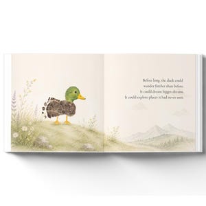 May include: An open children's book page featuring a watercolor illustration of a small duck with a green head and textured brown body standing on a grassy hill with wildflowers. The text reads: Before long, the duck could wander farther than before. It could dream bigger dreams. It could explore places it had never seen.