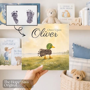 May include: A children's book titled Once Upon Oliver featuring an illustration of a duck with a body made of two dark gray baby footprints. The cover shows a green-headed duck in a grassy field under a bright sun, with the text The Story Of A Little Duck Named Oliver.