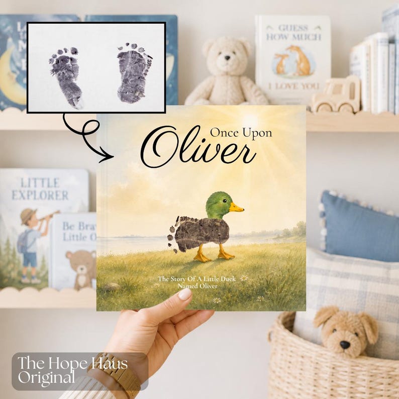 May include: A children's book titled Once Upon Oliver featuring an illustration of a duck with a body made of two dark gray baby footprints. The cover shows a green-headed duck in a grassy field under a bright sun, with the text The Story Of A Little Duck Named Oliver.