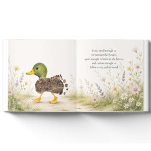 May include: An open children's book page featuring a watercolor illustration of a green and brown duckling walking through a field of wildflowers. The text reads: It was small enough to fit between the flowers, quiet enough to listen to the breeze, and curious enough to follow every path it found.