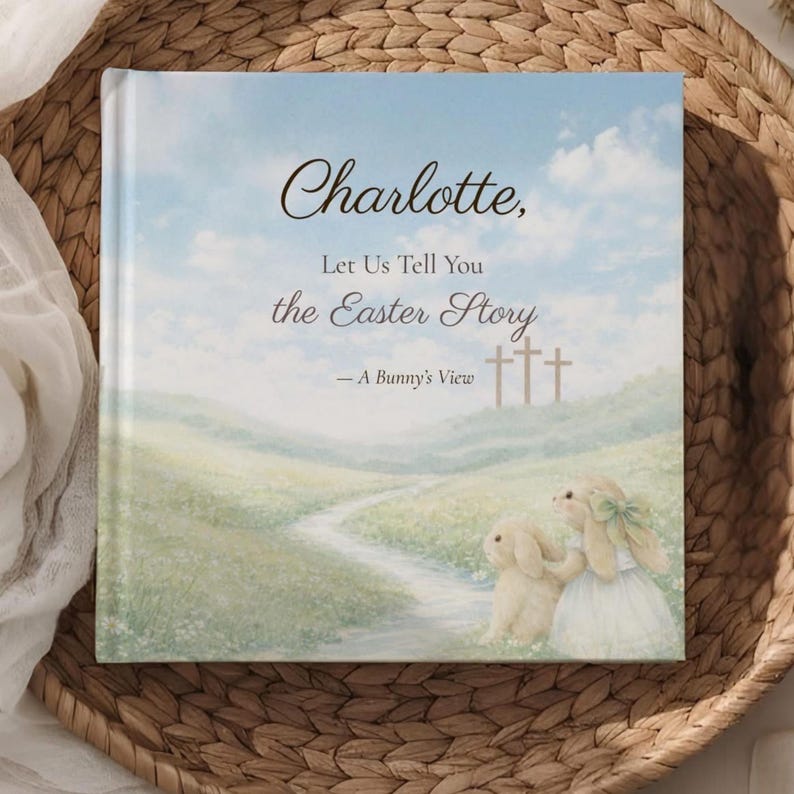 K&ouml;nnte beinhalten: Ein Kinderbuch mit dem Titel "Charlotte, Let Us Tell You the Easter Story - A Bunny's View." Das Cover zeigt eine pastellfarbene Landschaft mit einem Pfad, drei Kreuzen und zwei Hasenillustrationen. Das Buch liegt in einem geflochtenen Korb.