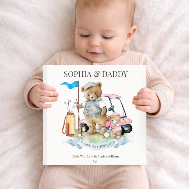 May include: A baby holds a personalized Father's Day card. The card features a watercolor illustration of two teddy bears on a golf course with a pink golf cart. Text on the card reads "SOPHIA & DADDY" and "HAPPY FATHER'S DAY".