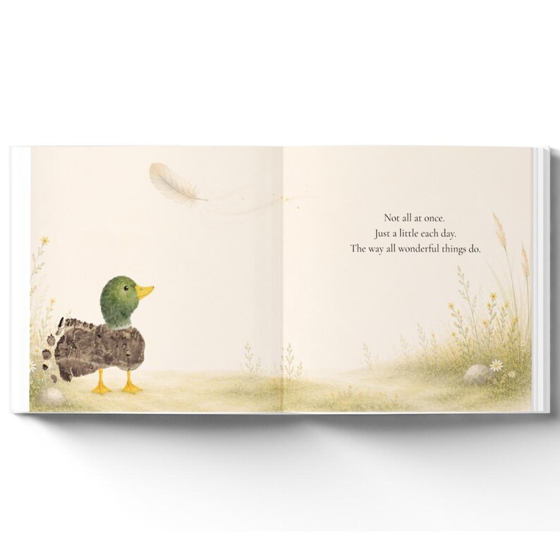 May include: An open book page featuring a watercolor illustration of a mallard duck with a green head and yellow feet standing in a grassy field. A single feather floats above. The text reads: Not all at once. Just a little each day. The way all wonderful things do.