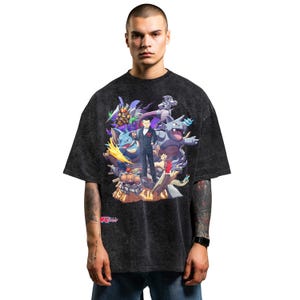 Puede incluir: Camiseta gris oscuro de gran tamaño con un gráfico colorido de varios personajes animados y un hombre con traje. El diseño incluye criaturas en tonos azules, morados y grises. La camiseta tiene un lavado vintage.