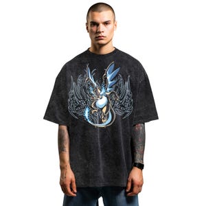 May include: Dark grey t-shirt with a dragon illustration in blue and white. The dragon has large wings and is surrounded by a decorative design. The shirt has a vintage, washed appearance, with a slightly oversized fit.