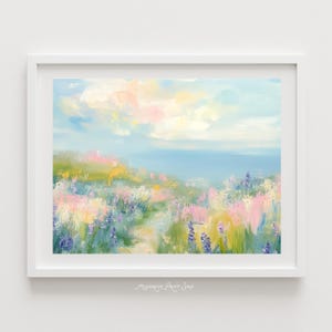 Puede incluir: Pintura de paisaje enmarcada con una serena escena costera. La obra presenta un campo de flores silvestres coloridas en tonos rosa, morado y amarillo, con un cielo azul suave y el océano al fondo. La pintura está en un marco blanco.