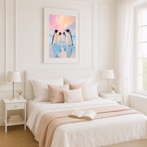 May include: A framed art print featuring three penguins standing on ice, set against a pastel sky. The artwork is displayed above a bed with white linens, blush pillows, and a matching throw blanket. A bedside table with a lamp is visible.