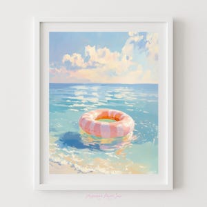 May include: A framed art print of a serene beach scene. The artwork depicts a pink and white striped inflatable ring floating in calm, turquoise water. The sky is a soft blue with fluffy white clouds, creating a peaceful summer vibe.