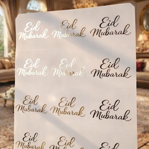 Puede incluir: Una hoja de pegatinas con la frase "Eid Mubarak" en letra cursiva. El texto es dorado, plateado y negro. Las pegatinas están dispuestas en filas y columnas sobre un fondo blanco.