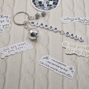 May include: A silver keyring featuring a miniature disco ball charm and the words "MIRROR BALL" spelled out in white letter beads. Stickers with quotes and a disco ball design are also visible.