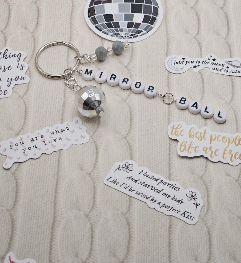 May include: A silver keyring featuring a miniature disco ball charm and the words "MIRROR BALL" spelled out in white letter beads. Stickers with quotes and a disco ball design are also visible.