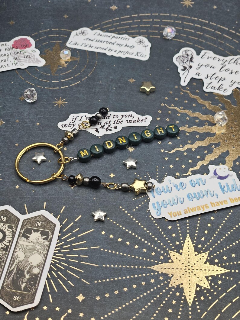 May include: A handmade keychain spelling "MIDNIGHT" in green and gold beads. It has a gold ring, star charms, and decorative beads. The background is dark with gold star and sunburst designs. Includes text stickers.