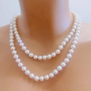 Puede incluir: Collar de perlas de dos hilos con un diseño clásico. Las perlas son de color blanco cremoso y de tamaño uniforme. El collar está drapeado alrededor de un cuello, mostrando la elegante simplicidad de la joya.