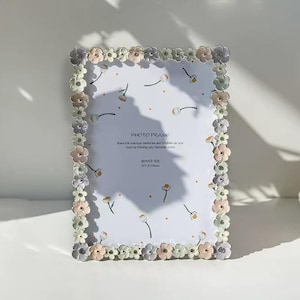 Puede incluir: Marco de fotos rectangular con borde floral en colores pastel. El marco tiene un fondo blanco con un diseño floral y el texto "PHOTO FRAME". El tamaño del marco es de 12,7 x 17,8 cm.