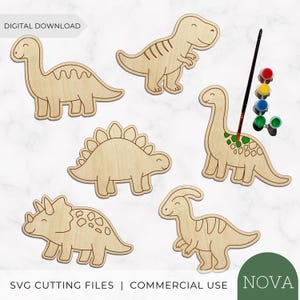 Könnte beinhalten: Sechs Holzausschnitte von Dinosauriern mit gravierten Umrissen, darunter ein Langhalsdinosaurier, ein T-Rex, ein Stegosaurus, ein Triceratops und ein Parasaurolophus. Ein Pinsel trägt grüne Farbe auf einen Dinosaurier auf, daneben stehen Farbtöpfe.