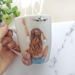 May include: White ceramic mug with a sculpted design of a woman with long brown hair, a backpack, and a small airplane. The woman is wearing a white shirt and denim shorts. The mug has a handle and is filled with a hot beverage.