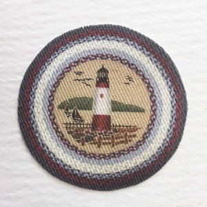 May include: A round, woven rug with a lighthouse, sailboat, and birds in a coastal scene. The rug has a red, white, and blue border.