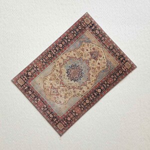 May include: A rectangular miniature rug with an intricate floral pattern. The rug features a central medallion in shades of blue and beige, surrounded by a border of red and black floral designs. The rug's overall color palette is muted, with a vintage aesthetic.