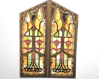 Puede incluir: Una ventana de vidrieras de dos paneles de madera con una parte superior puntiaguda. La ventana presenta un diseño con colores amarillo, naranja, rojo y verde. El marco de madera es marrón.