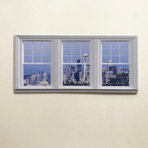 May include: A window view of the Seattle skyline with the Space Needle in the center. The cityscape is framed by a white window with multiple panes.