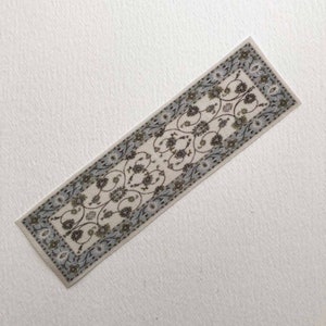 May include: A white runner rug with a blue and brown floral pattern. The rug has a border with a repeating design.