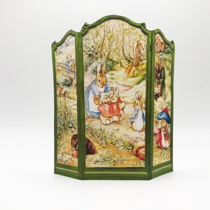 May include: A green three-panel room divider with a woodland scene featuring Peter Rabbit and his family. The divider is made of cardboard and has a vintage look.