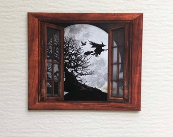 May include: A framed picture of a window with a full moon and two witches flying on broomsticks in the background.